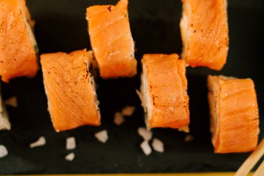 Lezzetli suşi ruloları siyah bir tabakta servis edilir. Yemek çubuklarıyla zevke hazır.