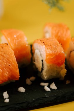 Taze somon suşisi ruloları, deniz tuzu kristalleriyle siyah bir tabakta servis edilir.