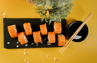 Parlak portakallı suşi ruloları yemek çubukları ve yeşillikle servis edilir.