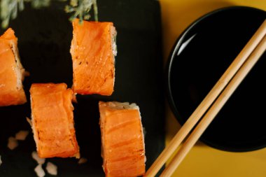 Taze suşi dürümleri, yemek için çubuklarla birlikte siyah bir tabağa yerleştirilmiş.