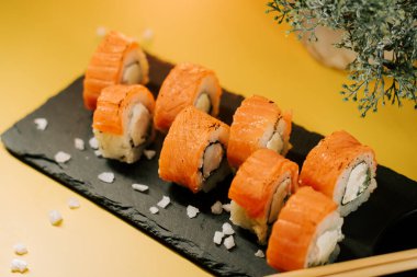 Taze suşi ruloları sarı arkaplanlı bir tabakta sergilenir.