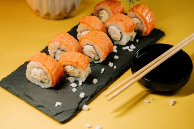 Soya soslu ve çubuklu siyah bir tabakta servis edilen lezzetli suşi ruloları.