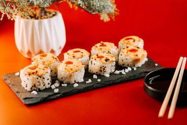 Lezzetli suşi ruloları ve siyah bir tabakta servis edilen baharatlı bir kapak.