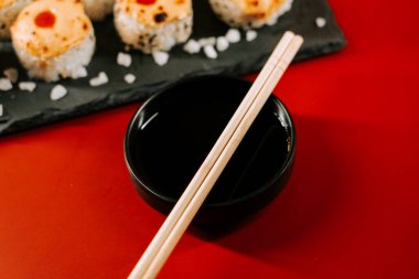 Suşi ve soya sosunu canlı kırmızı bir masada yemek çubuklarıyla yemek yemek.