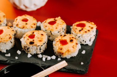 Eritilmiş peynirli lezzetli suşi ruloları ve siyah servis tabağında baharatlı sos.