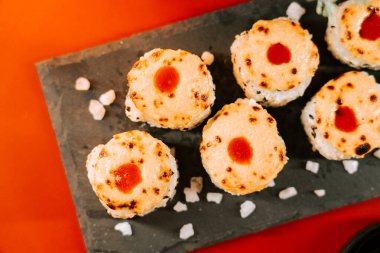 Erimiş peynir ve sosla birlikte siyah bir tabakta eşsiz suşi ruloları.