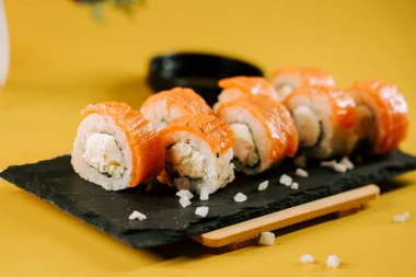 Siyah bir tabakta servis edilen somon ve krem peynirli taze suşi ruloları.