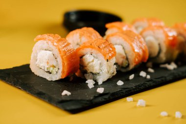 Suşi, parlak sarı bir arka planda somon balığı tabağında yuvarlanır.