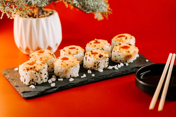 Lezzetli suşi ruloları ve siyah bir tabakta servis edilen baharatlı bir kapak.
