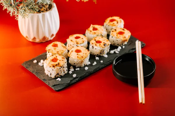 Parlak renkli suşi ruloları siyah taştan bir tabakta sos ve çubuklarla servis ediliyor.