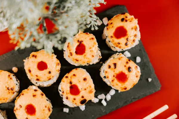 Canlı bir restoran ortamında siyah bir tabakta servis edilen soslu suşi ruloları.