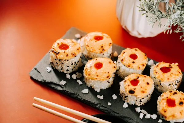 Modern bir restoranda siyah bir tabakta servis edilen lezzetli pişmiş suşi.