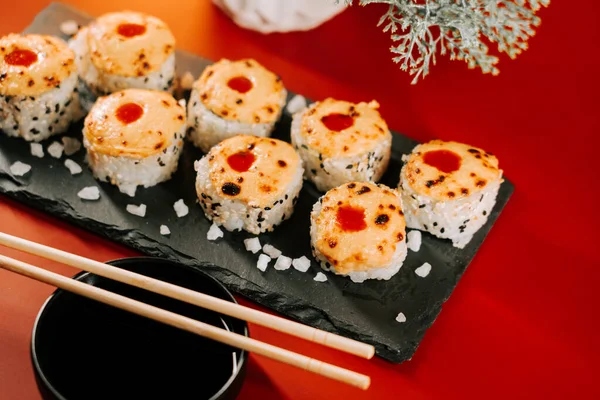 Nefis bir şekilde hazırlanmış suşi dürümleri yemek çubuklarıyla servis edilmiş siyah taş bir tabakta.