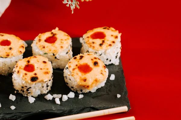 Kırmızı arka planda siyah tabakta servis edilen eritilmiş soslu lezzetli suşi ruloları.