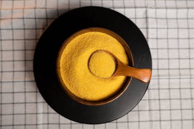 Tahta bir kasede mısır ezmesi ve siyah bir tabakta bir kaşık kareli bir kumaş.