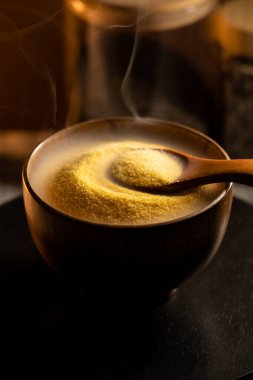 Sıcak bir mutfakta ahşap kaşıkla karıştırılmış mısır gevreğinden buhar yükselir.