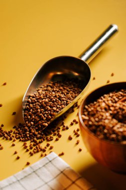 Karabuğday, sarı yüzeydeki ahşap kasenin yanında metal kepçeyle inliyor.