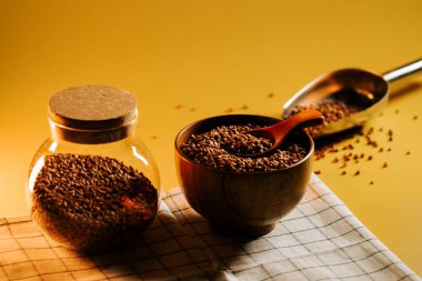 Karabuğday ahşap kasede ve kavanozda kareli kumaş üzerinde kaşık ve sarı arka planda inliyor.