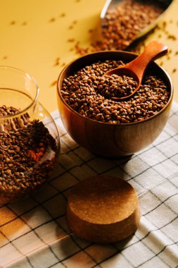 Karabuğday ahşap kasede, kepçe ve kareli kumaş kavanozuyla homurdanıyor.