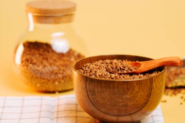 Karabuğday, sarı arka planda bir kavanozun yanında ahşap bir kasede inliyor.