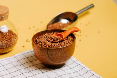 Karabuğday, sarı arka planda bir kaşıkla ahşap bir kasede inliyor ve sağlıklı taneler sergiliyor.