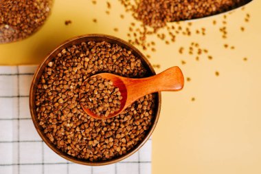 Karabuğday, sarı arka planda kaşıkla ahşap bir kasede inliyor.