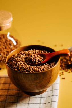 Karabuğday, sarı arka planda kaşıkla ahşap kasede inliyor.