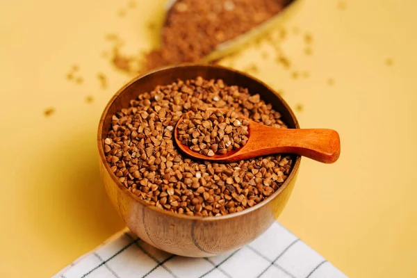 Karabuğday, sarı arka planda tahta kaşıkla bir kasede inliyor.