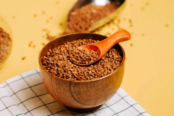 Karabuğday, sarı arka planda kaşıkla ahşap bir kasede inliyor.