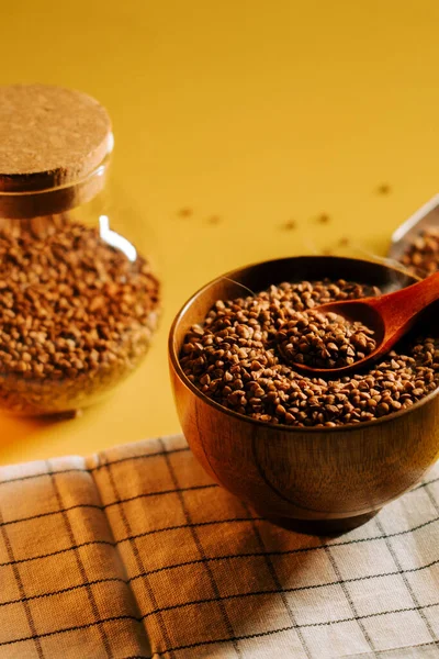 Karabuğday filizleri ahşap bir kasede sergilenir. Sarı arka planda bir kaşıkla.