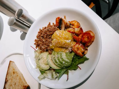 Parlak bir kafe ortamında karides, avokado ve tahıllı lezzetli deniz ürünleri kasesi.