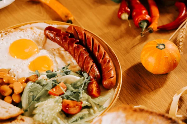 Kahvaltı yumurta, sosis ve taze sebzelerle ahşap bir masada.