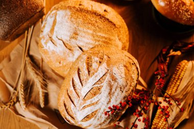 Mevsimlik dekor ve doğal elementlerle ahşap bir masada sergilenen taze zanaatkar ekmeği.