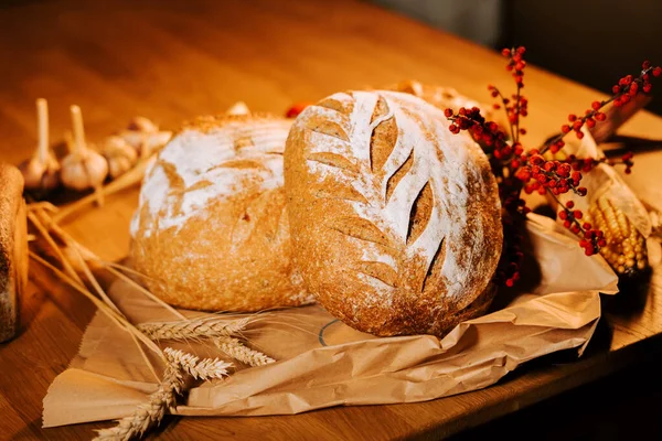 Taze zanaatkar ekmeği ahşap bir masada renkli bir sonbahar dekoru ve doğal elementlerle sergileniyor.