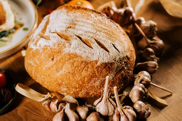 Sarımsak ve sebzelerle birlikte sade ahşap bir masaya yerleştirilmiş taze zanaatkar ekmeği.
