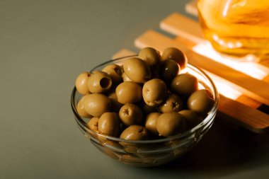 Düz bir yüzeyde, sıcak bir ışık kaynağının yanında, temiz bir kasede yeşil zeytinler.