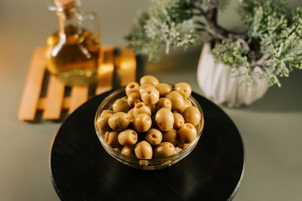 Zeytinyağlı cam bir kasede zeytin ve arka planda dekoratif bir bitki.