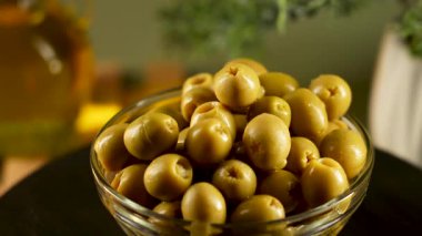 Parlak bir mutfaktaki ahşap bir masaya yerleştirilmiş cam bir kasede zeytin çeşitleri.