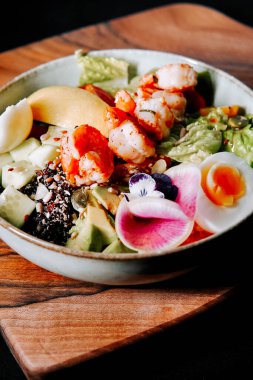 Tahta bir tabakta servis edilen taze ve renkli karides salatası.