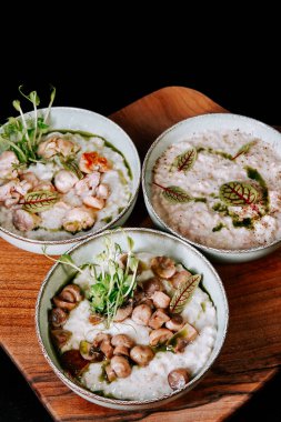 Üç kase kremalı çorba, deniz mahsulleri ve ahşap tabakta yeşil süslemeler.