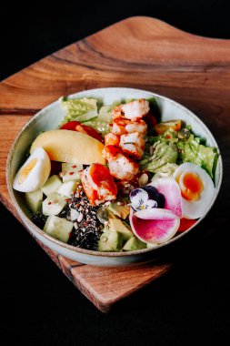 Tahta bir tahtanın üzerinde çeşitli sebzeler, proteinler ve yenilebilir çiçeklerle servis edilen sağlıklı salata kasesi.