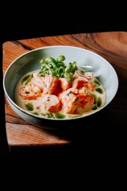 Kremalı sosta servis edilen taze karides ve ahşap tahtada otlar.