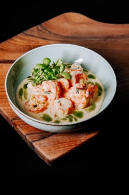 Sütlü soslu karides ahşap bir tahtanın üstünde şık bir kasede servis edilir.