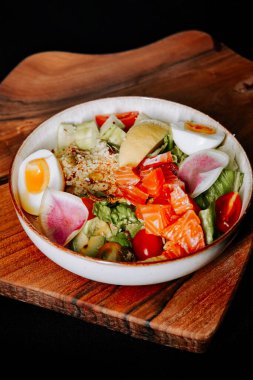 Tahta masada servis edilen somon, sebze ve yumurtalı taze salata kasesi.