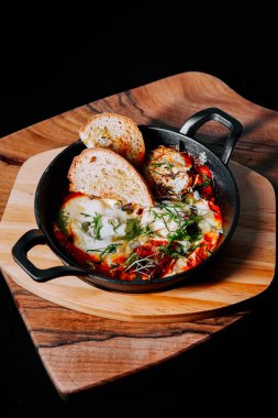 Domatesli nefis pişmiş yumurta ve ahşap tabakta kızarmış ekmekle servis edilen otlar.