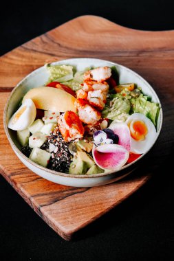 Tahtada karides, sebze ve yumurta bulunan renkli salata.