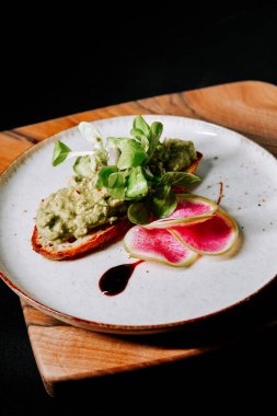 Taze yeşillik ve turp dilimleriyle süslenmiş lezzetli avokado tostu.