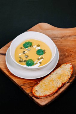 Kremalı çorba, ahşap kesme tahtasında yeşil garnitürlü kızarmış ekmekle servis edilir.