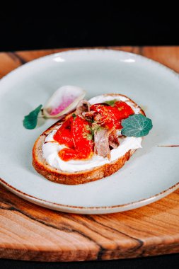 Ahşap bir tahtanın üzerinde kavrulmuş biber ve otlarla süslenmiş nefis açık yüzlü sandviç.