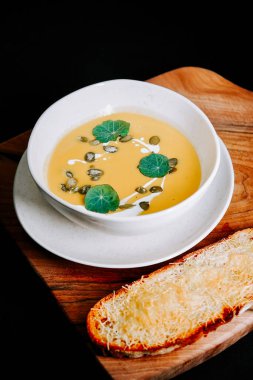 Tahtada peynirli tost ekmeğiyle servis edilen lezzetli kremalı çorba kasesi.